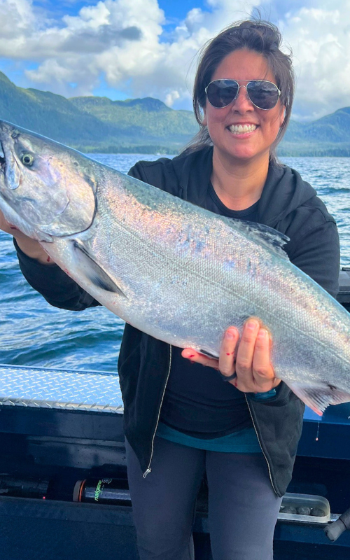 A woman on a boat holding a massive wild salmon.