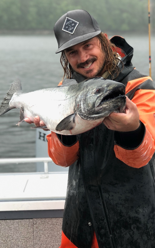 Captain Lukas of Ketchikan Finest Fishing Charters & Ketchikan Fishing Company holding a massive salmon in the rain.