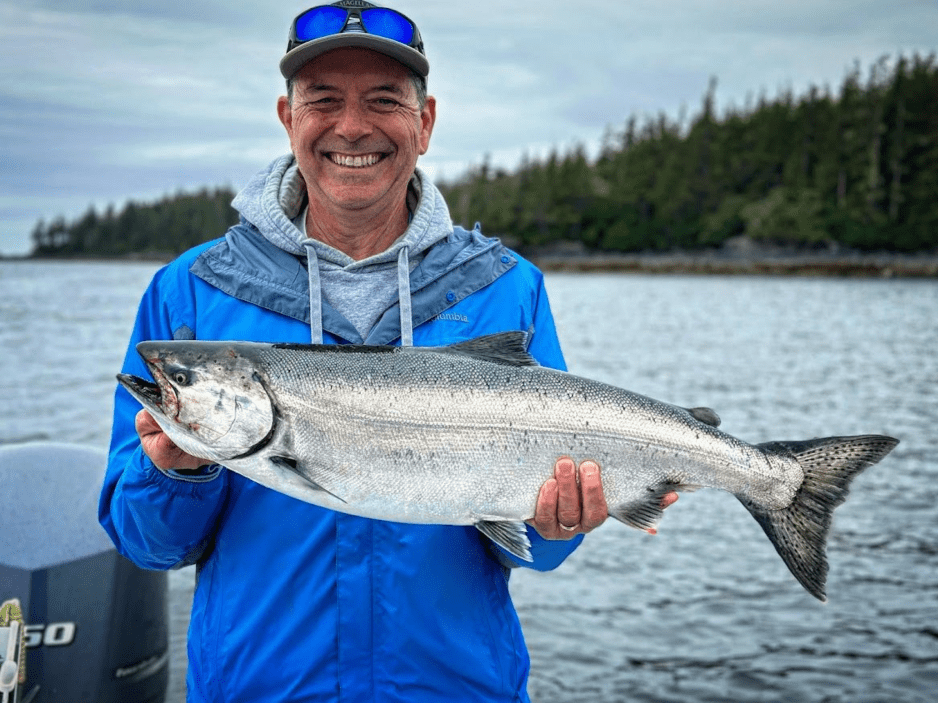 A guy holding a wild alaskan salmon that was caught out on a ketchikan fishing company charter.