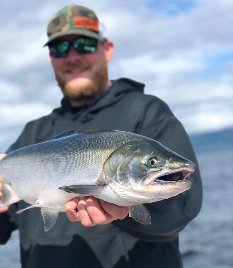 A guy holding a salmon out on the water during a fishing charter.