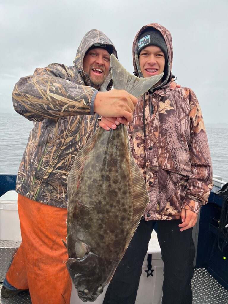 A father and son holding a massive pacific halibut that was caught fishing in ketchikan alaska.