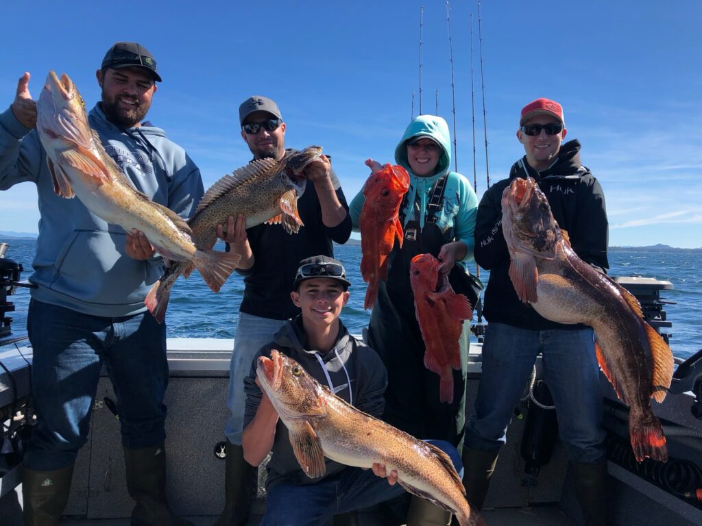 A group of 5 individuals standing on a boat holding massive lingcod that were caught during a ketchikan fishing charter.