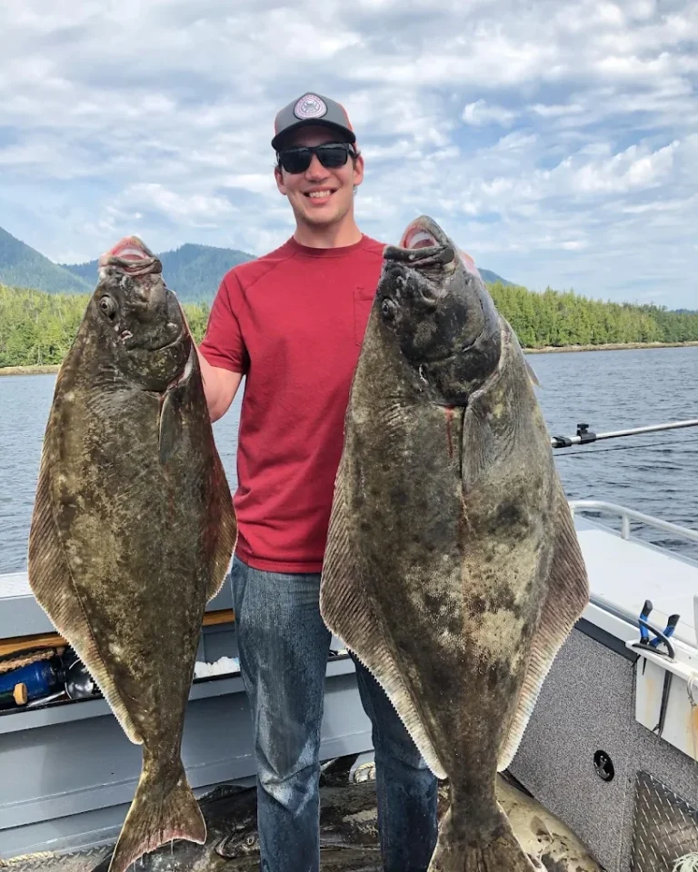 A guy holding 2 massive pacific halibut that were caught while fishing in ketchikan.