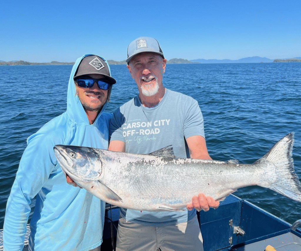 Captian Lukas of Ketchikan Fishing Company standing next to a first time angler holding a massive king salmon on a sunny day.