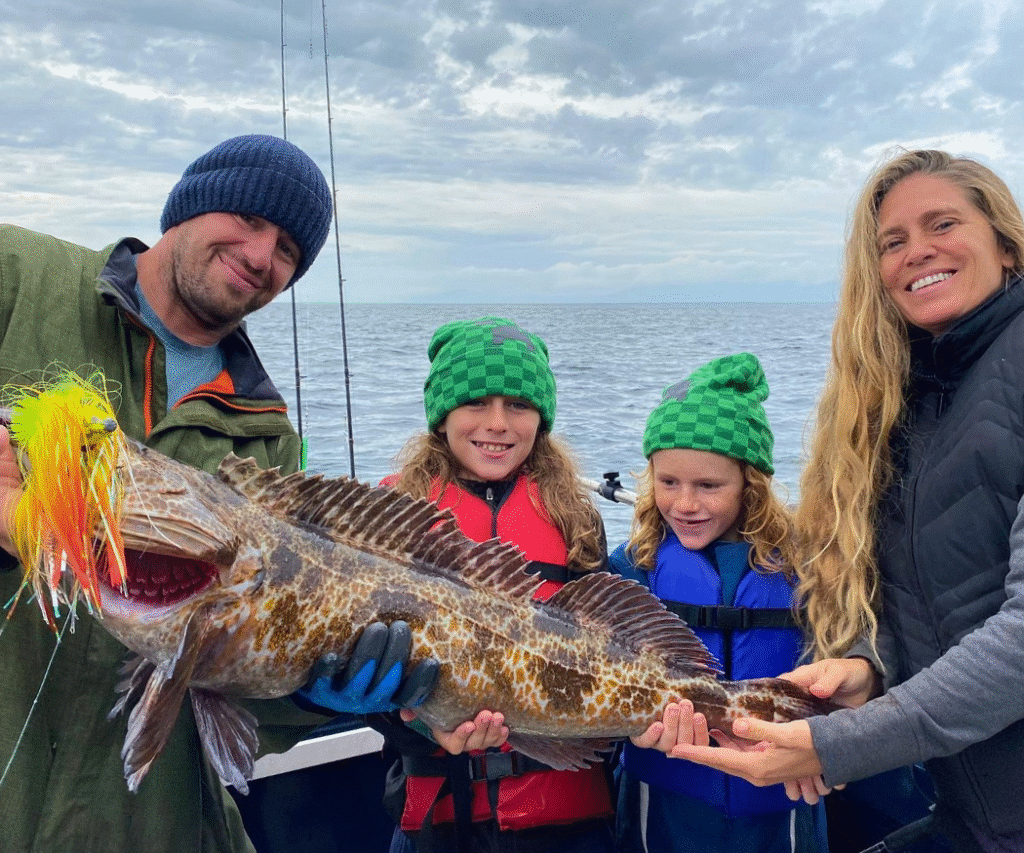 A Family of 4 on Ketchikan fishing charter holding a massive lingcod on a cloudy day