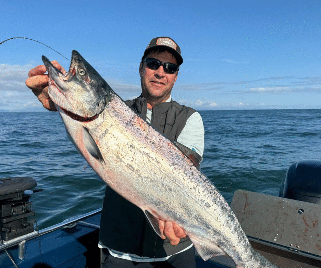 A guy holding a huge king salmon on a sunny day in Ketchikan Alaska.