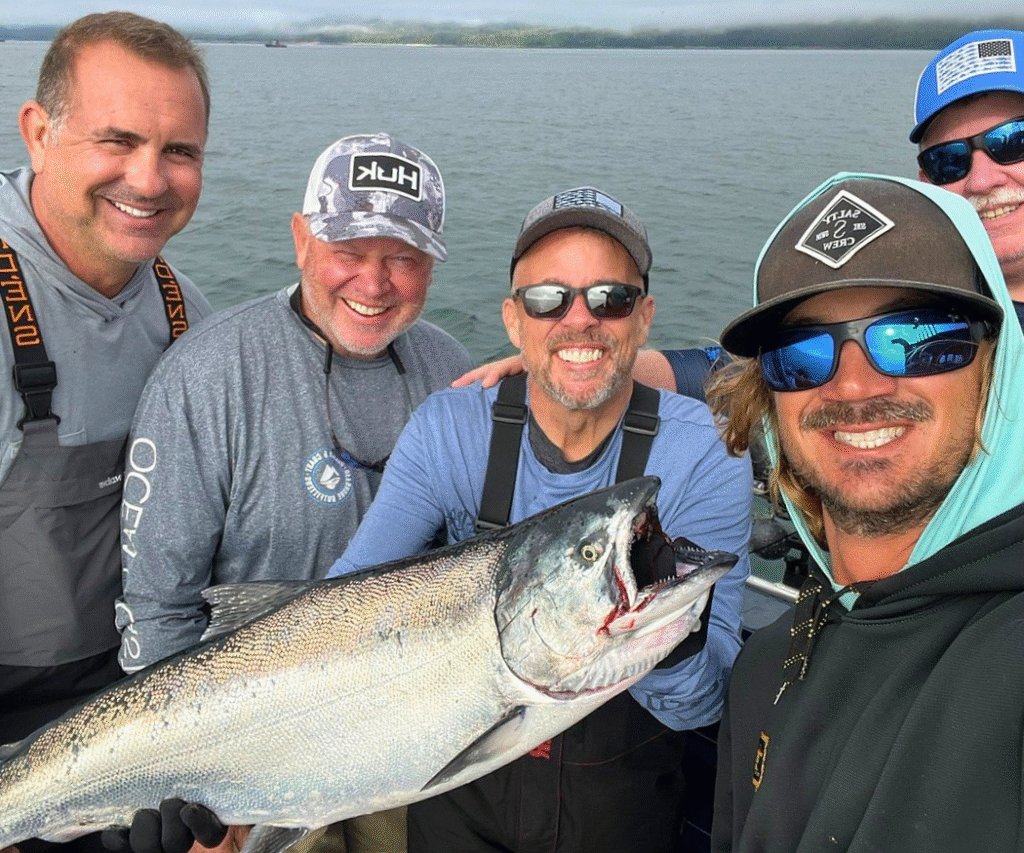 Captain Lukas of Ketchikan Fishing Company taking a selfie photo with a group of 4 guys holding a massive salmon.