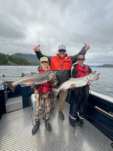 Captain Tony standing with 2 people holding massive salmon on a cloudy day
