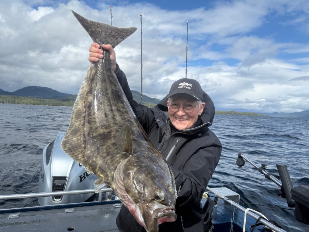 A woman holding a gigantic halibut in Ketchikan Alaska on a sunny day
