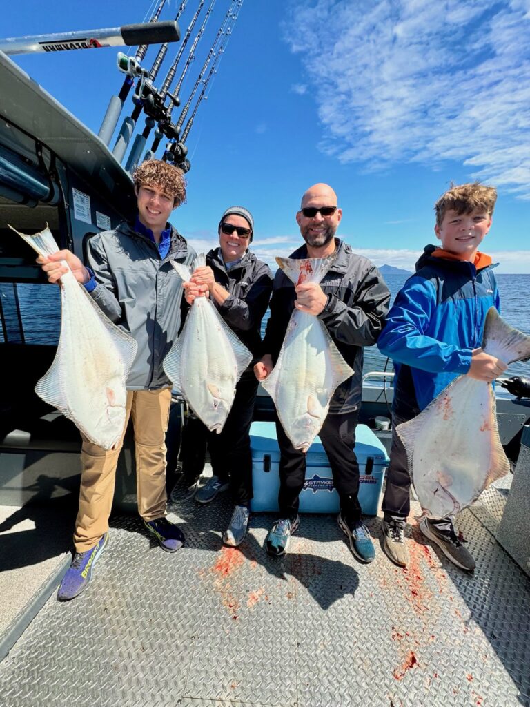 A family of 4 standing on a ketchikan fishing charter boat on a sunny day with huge halibuts in their hands.