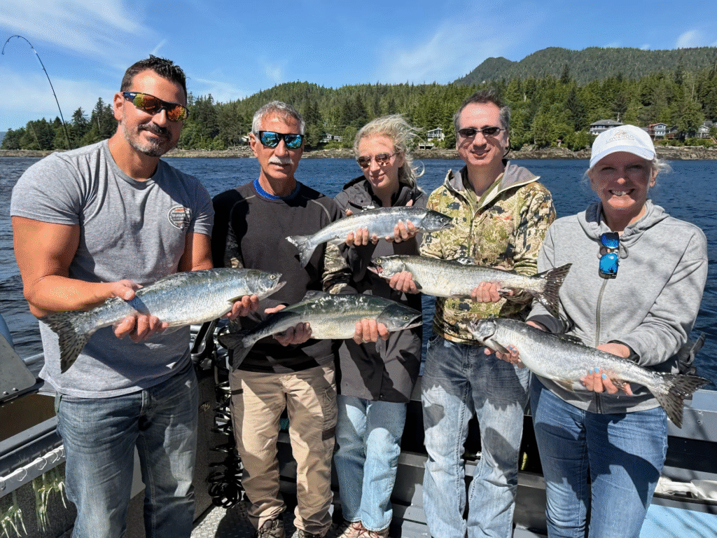 A group of smiling cruise guests on a sunny day proudly displays their fresh-caught salmon during a charter trip with Ketchikan’s Finest Fishing Charters + Ketchikan Fishing Company, part of the best Alaska cruise excursion experience.